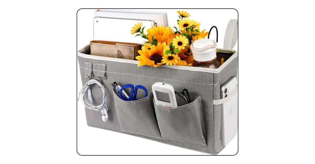 Grey fabric bedside caddy hanging from dorm bed rail with phone glasses chapstick and small book in pockets