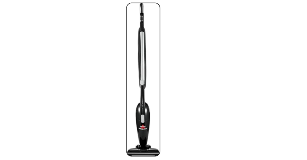 Black Bissell Featherweight stick vacuum leaning against dorm room wall near desk with crevice tool attached and clean organized room around it
