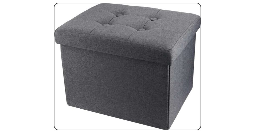 Grey rectangular storage ottoman at foot of college dorm bed with lid slightly open showing folded blanket inside used as footrest and storage
