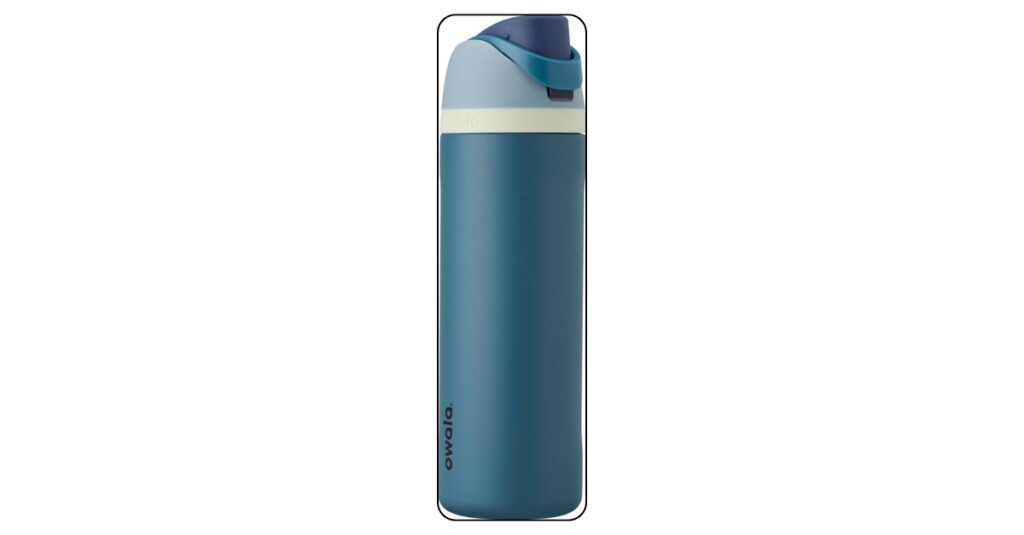 Owala FreeSip insulated water bottle in denim blue sitting on college desk beside open textbook and laptop with soft daylight from window