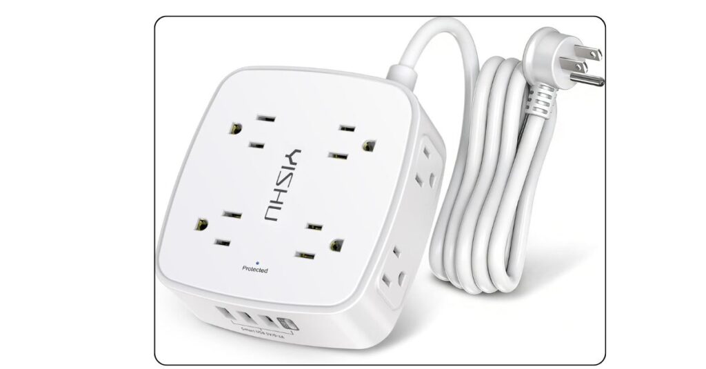 White flat plug surge protector power strip mounted along dorm room baseboard with multiple devices plugged in including laptop charger and phone cable
